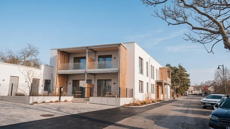 Modernes Mehrfamilienhaus mit weißer Fassade, Holzdetails und Balkonen an einer ruhigen Straße.