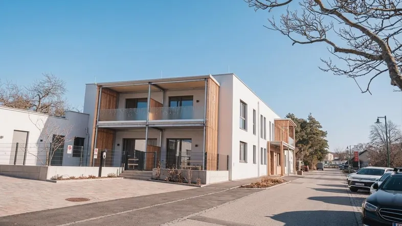 Modernes Mehrfamilienhaus mit Balkonen und Holzverkleidung unter blauem Himmel.