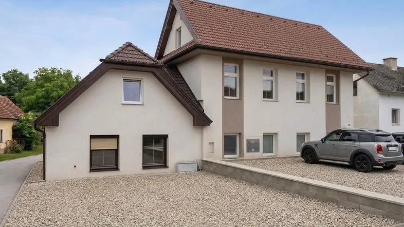Modernes Einfamilienhaus mit Satteldach, heller Fassade und Kiesparkplatz für Fahrzeuge.