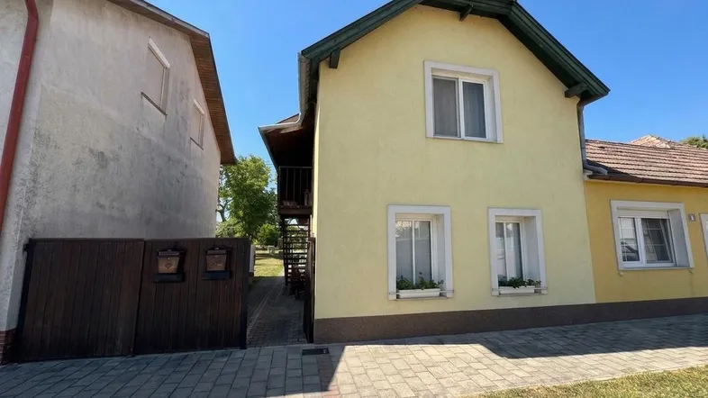 Gelbes Einfamilienhaus mit grünen Dachdetails und gepflastertem Zugangsweg unter blauem Himmel.
