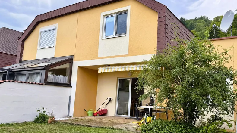 Hinteransicht des Hauses mit kleiner Terrasse, Gartenbereich und ausziehbarer Markise.