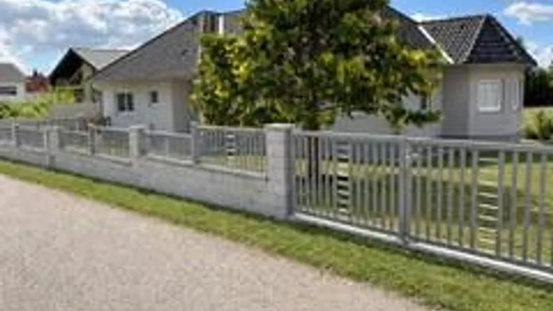 Modernes Einfamilienhaus mit gepflegtem Vorgarten und Zaun unter blauem Himmel.
