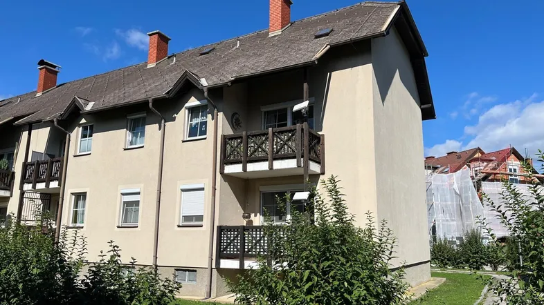 Mehrfamilienhaus mit beiger Fassade, Satteldach und kleinen Balkonen, umgeben von Grünflächen.