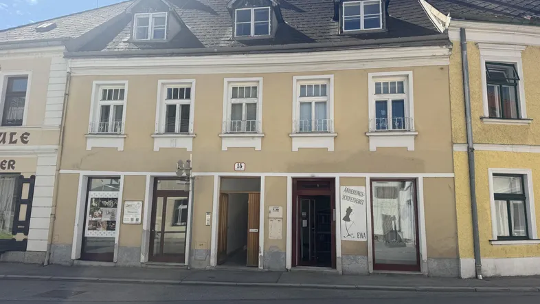 Fassade eines Mehrfamilienhauses mit Geschäften im Erdgeschoss und Dachgauben in gutem Zustand.