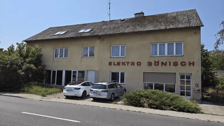 Gebäudeansicht eines älteren Hauses mit Geschäftsfassade und parkenden Autos davor.