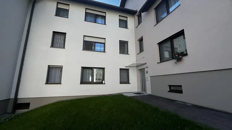 Mehrfamilienhaus mit heller Fassade, gepflegtem Vorgarten und Zufahrt.