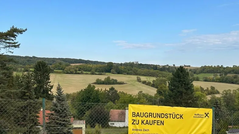 Blick auf ein Baugrundstück mit weitreichender grüner Landschaft und einem Verkaufsschild im Vordergrund.