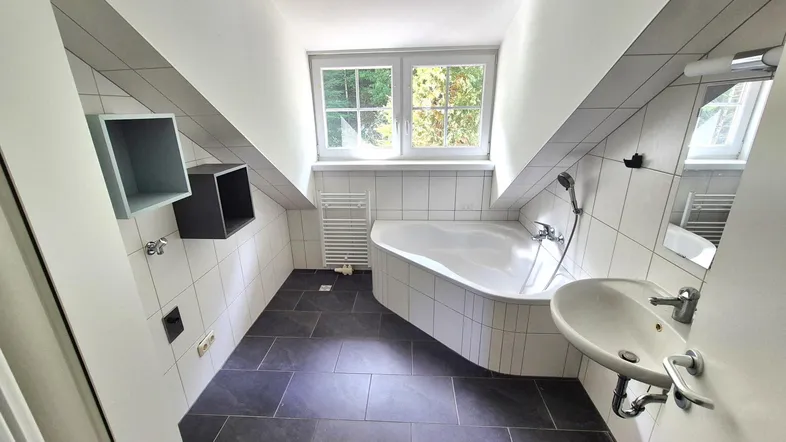 Modernes Badezimmer mit Badewanne, Waschbecken und Fenster unter einer Dachschräge.