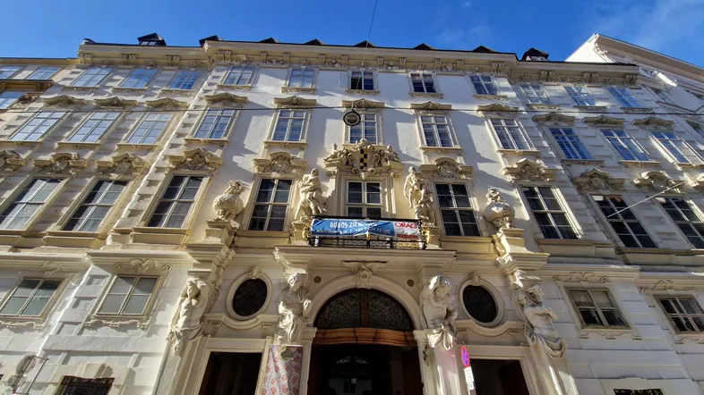 Prachtvolle historische Fassade eines Gebäudes mit vielen Fenstern und aufwendigen Verzierungen unter blauem Himmel.