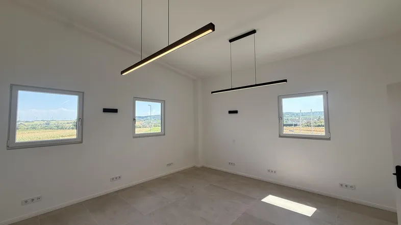 Heller, leerer Raum mit großen Fenstern, die einen weiten Blick auf die Landschaft bieten und modernen Pendelleuchten.