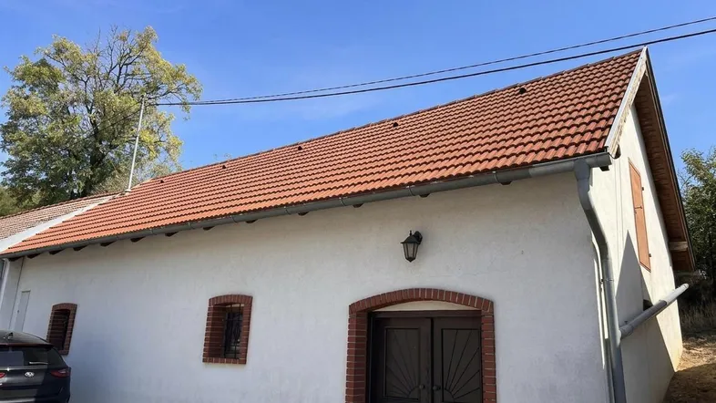 Seitenansicht eines traditionellen Gebäudes mit weißer Fassade, rotem Ziegeldach und kleinen Fenstern unter blauem Himmel.