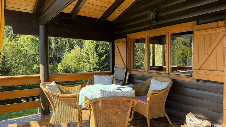 Überdachter Balkon mit Korbmöbeln und Blick ins Grüne, ideal zum Entspannen.