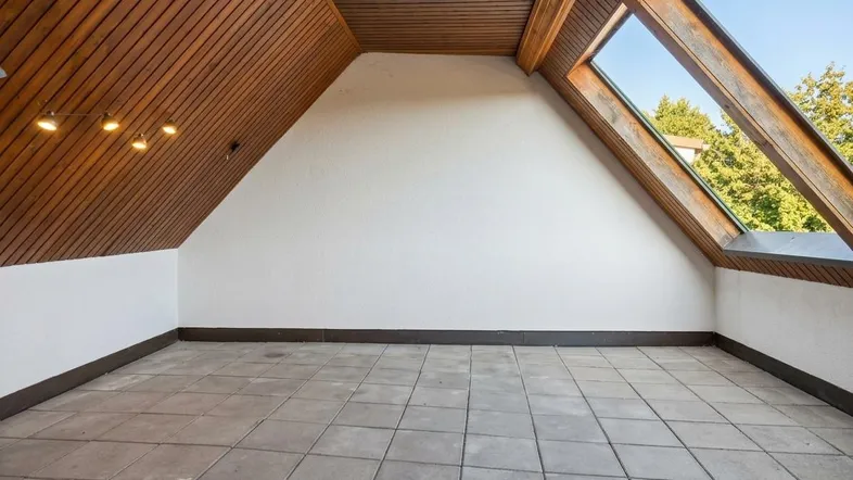 Geräumiger Dachbodenraum mit Holzbalkendecke, Fliesenboden und großem Dachfenster.