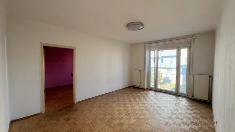 Helles Wohnzimmer mit Parkettboden und Zugang zu einem weiteren Raum sowie einem Balkon.