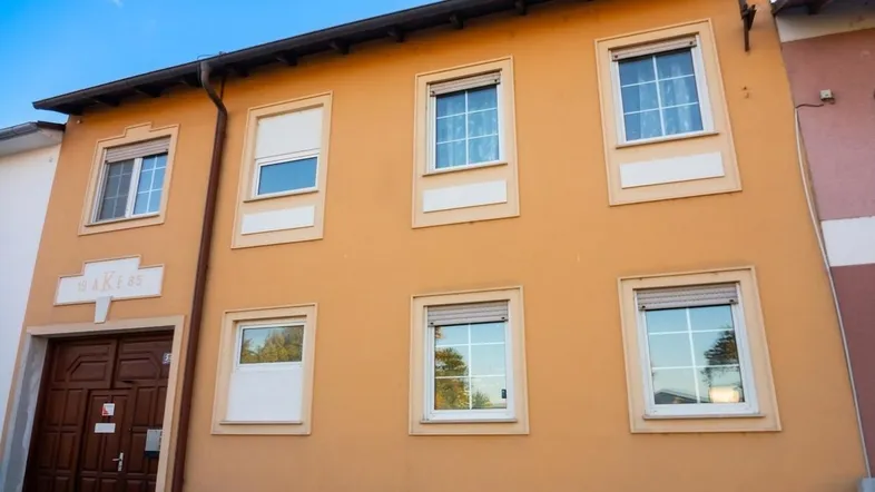 Fassade eines Wohnhauses mit mehreren Fenstern, Rollläden und einem Garagentor.