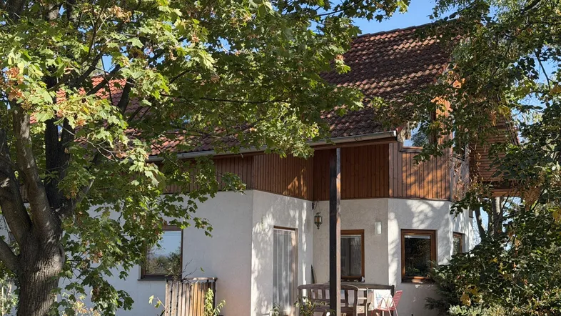Charmantes Einfamilienhaus mit Holzverkleidung und gemütlicher Terrasse umgeben von viel Grün.