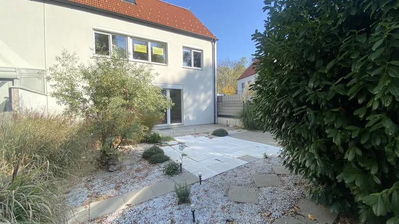 Hinteransicht eines modernen Hauses mit gepflasterter Terrasse und einem pflegeleichten Gartenbereich.
