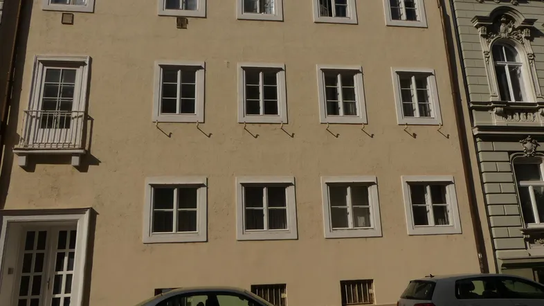 Fassade eines Mehrfamilienhauses mit mehreren Fenstern und einem kleinen französischen Balkon.
