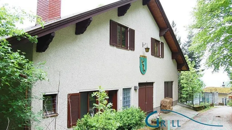 Traditionelles Haus mit Satteldach, braunen Fensterläden und einem Kamin in ländlicher Umgebung.