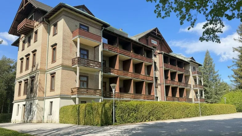Mehrstöckiges Gebäude mit Ziegelfassade, Holzbalkonen und gepflegter Hecke unter blauem Himmel.