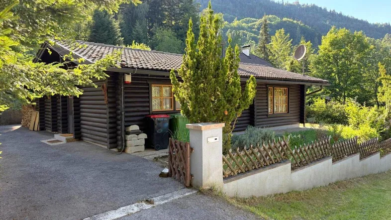 Rustikales Holzhaus im Blockhausstil mit Auffahrt und Blick auf die umliegende Berglandschaft.