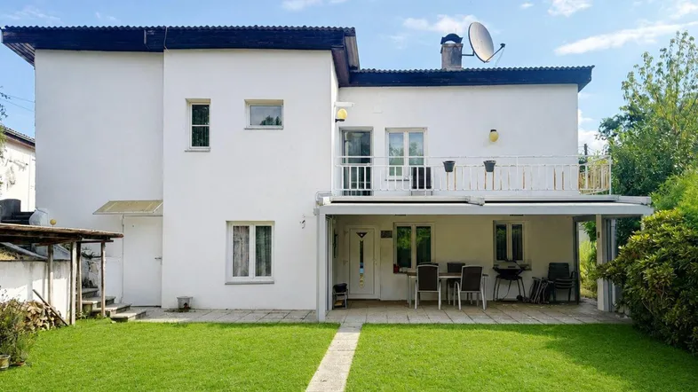Weißes Einfamilienhaus mit großem Garten, überdachter Terrasse und Balkon im Obergeschoss.