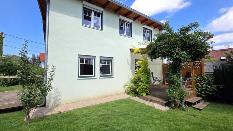Seitlicher Blick auf das Haus mit gepflegtem Rasen und einer kleinen Holzterrasse im Gartenbereich.