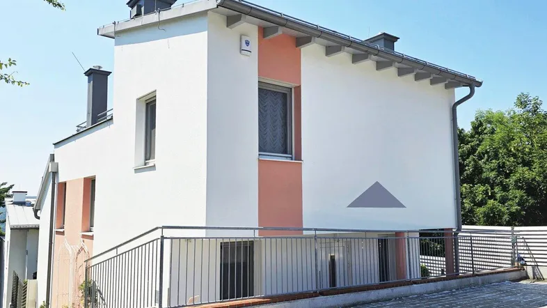 Modernes Einfamilienhaus mit weißer Fassade und Akzenten in Terrakotta, umgeben von einer niedrigen Mauer und Geländer.