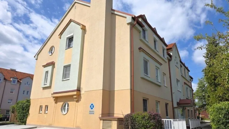 Mehrfamilienhaus mit heller Fassade und Parkplätzen im Freien unter blauem Himmel.
