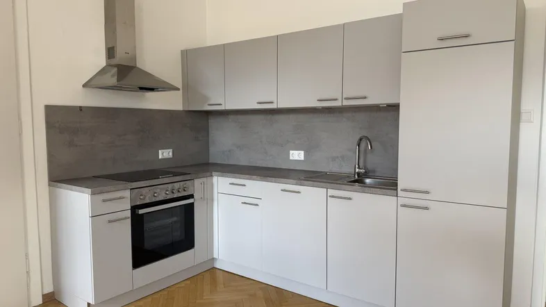 Moderne Einbauküche in Grau mit Induktionskochfeld, Backofen und Fischgrätparkettboden.