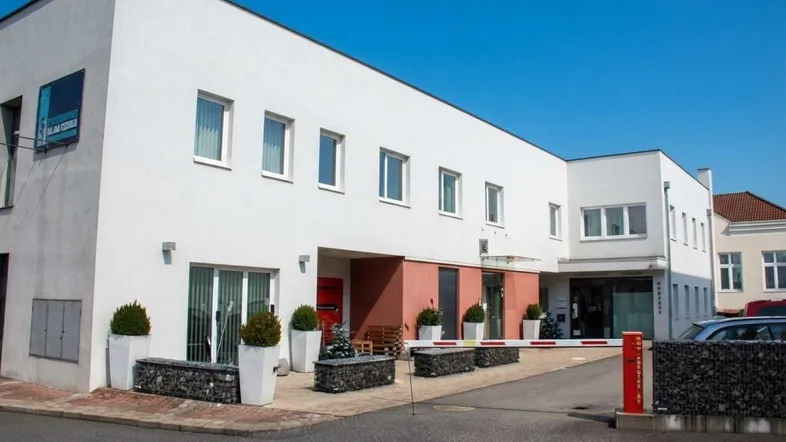 Modernes Gebäude mit weißer Fassade, großen Fenstern und gepflegtem Eingangsbereich.