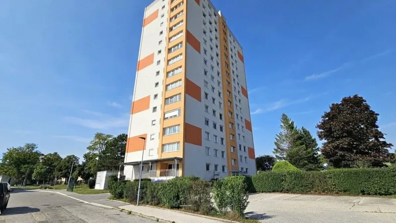 Hohes Wohngebäude mit weißer und orangefarbener Fassade unter blauem Himmel.