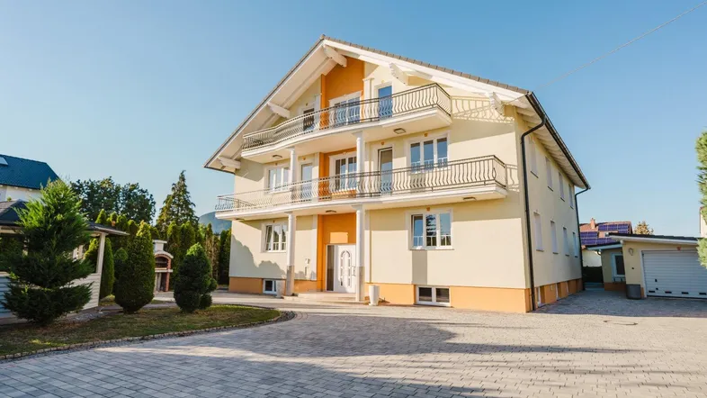 Großzügiges Einfamilienhaus mit mehreren Balkonen, gepflasterter Auffahrt und Garage im Sonnenlicht.