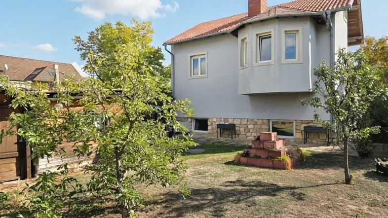 Hausfassade mit Gartenbereich und Obstbäumen unter blauem Himmel.