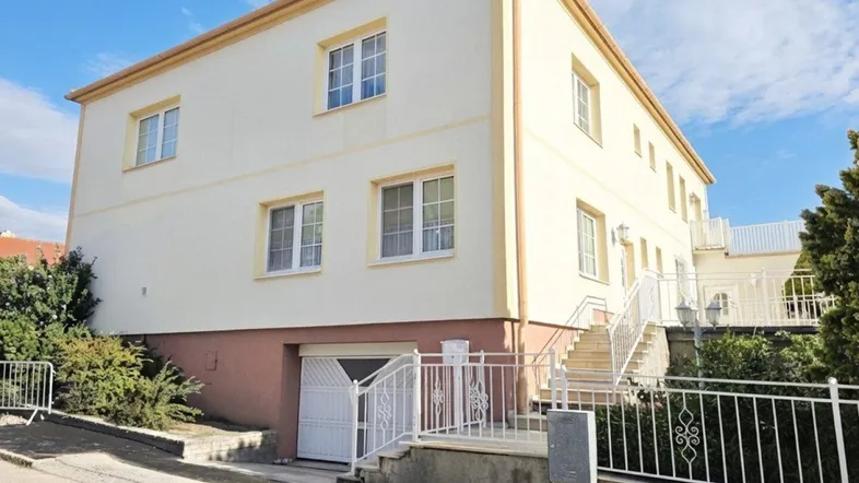 Großes Wohnhaus mit mehreren Etagen, Garage im Untergeschoss und weißem Zaun an der Straße.