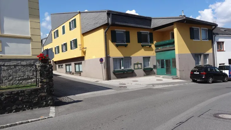 Gelbes Gebäude mit grauen Dächern und grünen Fensterläden an einer Straßenecke.