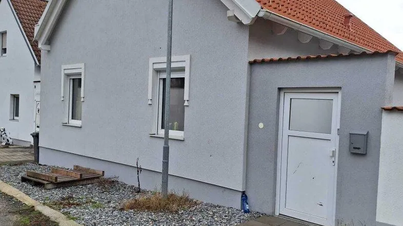 Vorderansicht eines modernen Einfamilienhauses mit hellgrauer Fassade und rotem Ziegeldach.