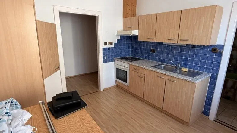 Funktionale Küche mit hellen Holzschränken, blauen Fliesen und einem Esstisch.