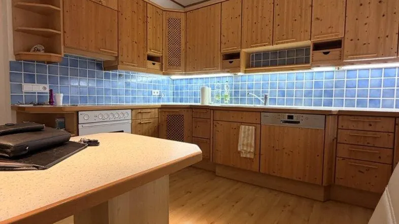 Gemütliche Küche mit Holzschränken, blauen Fliesen und integrierten Geräten, ideal für den täglichen Gebrauch.