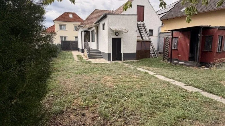 Blick auf das Haus von einem ungepflegten Garten aus, mit einer Außentreppe und einem Nebengebäude.