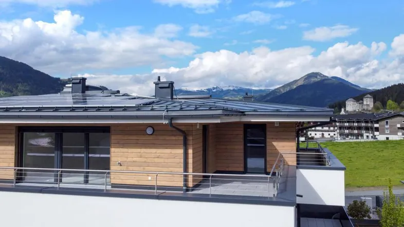 Modernes Gebäude mit Holzfassade, Solaranlage auf dem Dach und Bergblick.