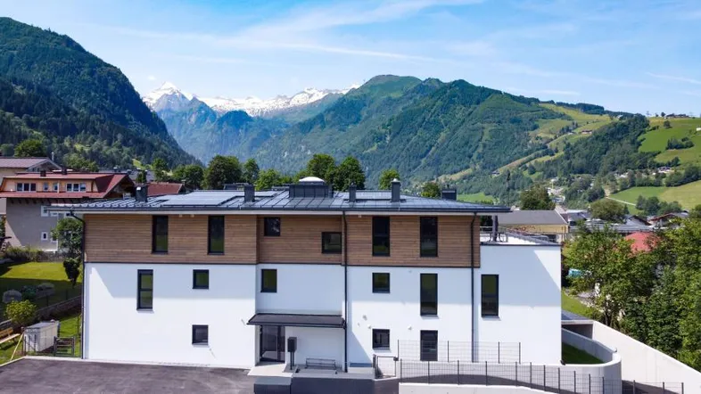 Modernes Mehrfamilienhaus mit Holzfassade und beeindruckendem Bergblick in grüner Umgebung.
