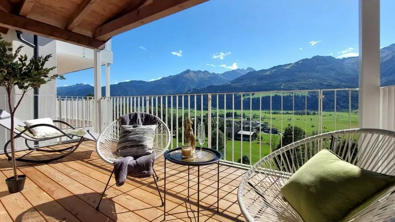 Überdachter Balkon mit Holzboden, gemütlichen Sitzgelegenheiten und weitem Bergblick.