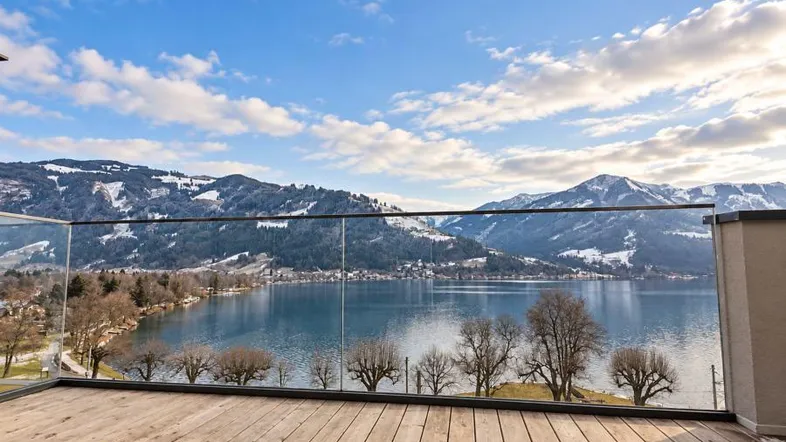 Große Holzterrasse mit Glasgeländer bietet einen atemberaubenden Blick auf den See und die schneebedeckten Berge.
