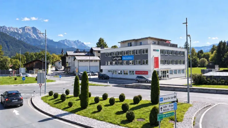 Modernes Bürogebäude an einem Kreisverkehr mit Bergpanorama im Hintergrund unter blauem Himmel.