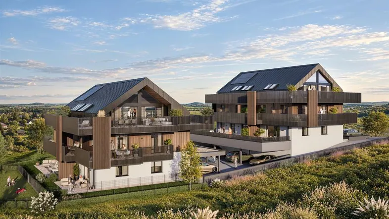 Moderne Mehrfamilienhäuser mit Satteldach, Balkonen und Terrassen, eingebettet in eine grüne Landschaft.
