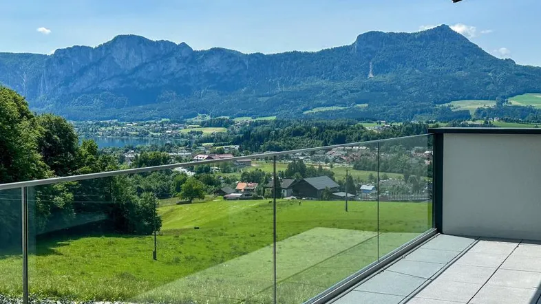 Geräumiger Balkon mit Glasgeländer und atemberaubendem Blick auf den See und die umliegende Berglandschaft.