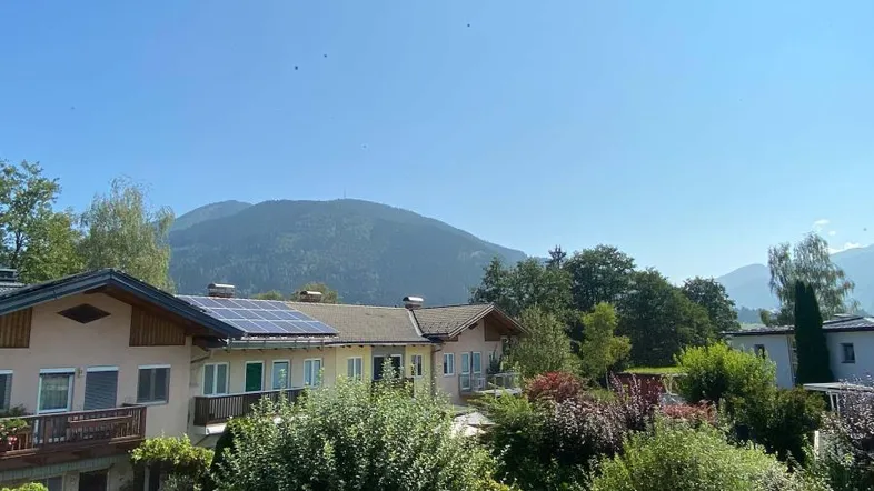 Blick auf das Gebäude mit Solaranlage und grüner Umgebung vor einer beeindruckenden Bergkulisse.