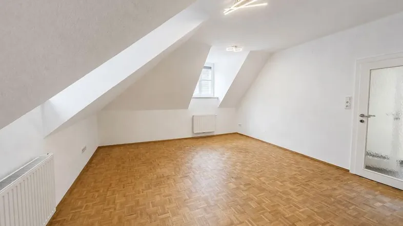 Helles Zimmer im Dachgeschoss mit Parkettboden und schrägen Wänden, ideal als Schlafzimmer nutzbar.
