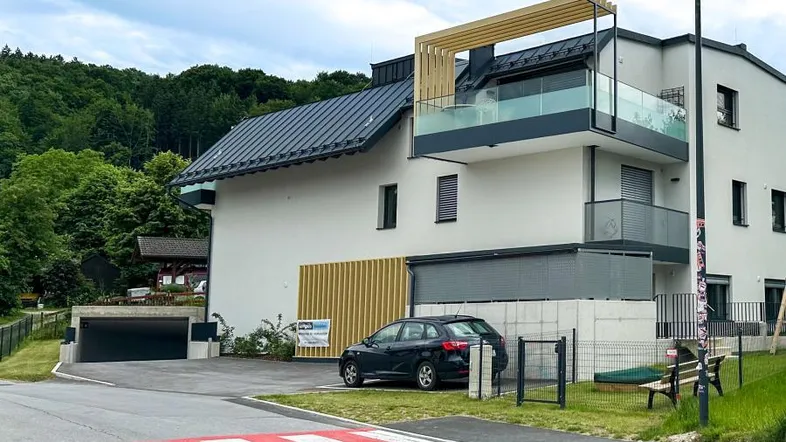 Modernes Mehrfamilienhaus mit Balkonen, Glasgeländern und Tiefgaragenzufahrt, umgeben von viel Grün.